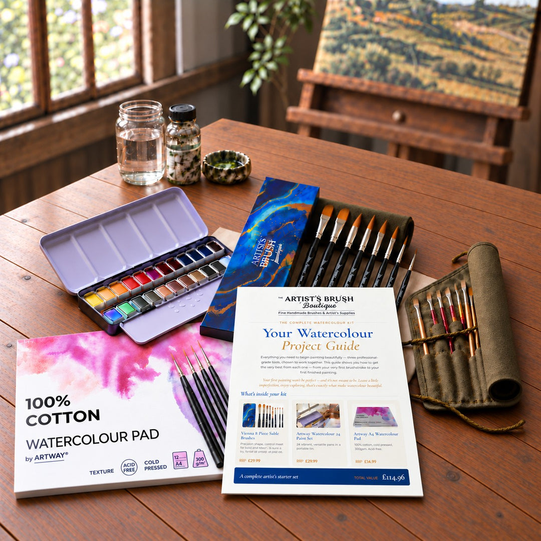 The Complete Watercolour Kit on an oak table: 24 half-pan watercolour tin, Vienna 8-piece sable brush set, 100% cotton A4 watercolour pad, Finesse detail brushes, brush roll and project guide